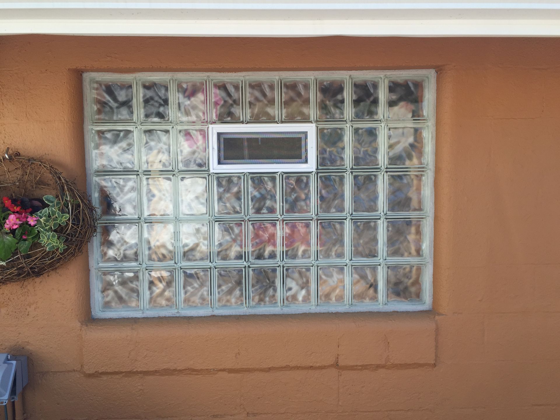 Glass block window with a small rectangular window set in an orange stucco wall.