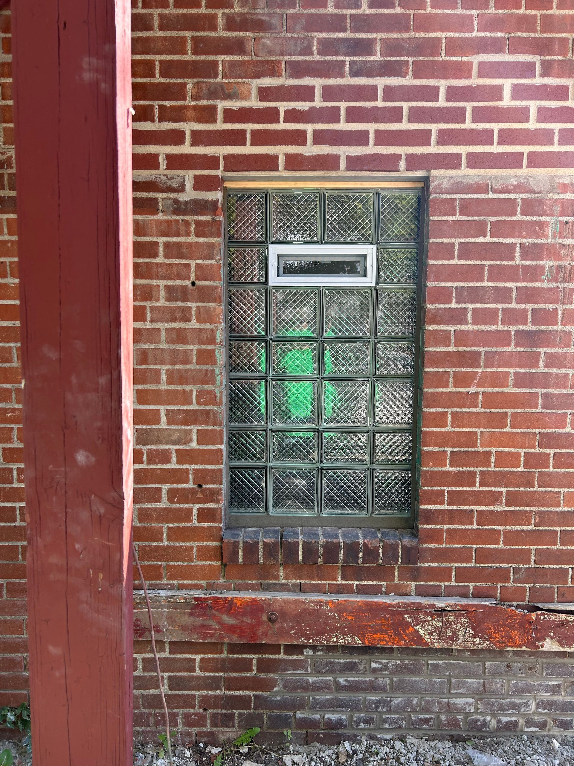 Red brick building with glass block window; a red wooden post stands on the left.