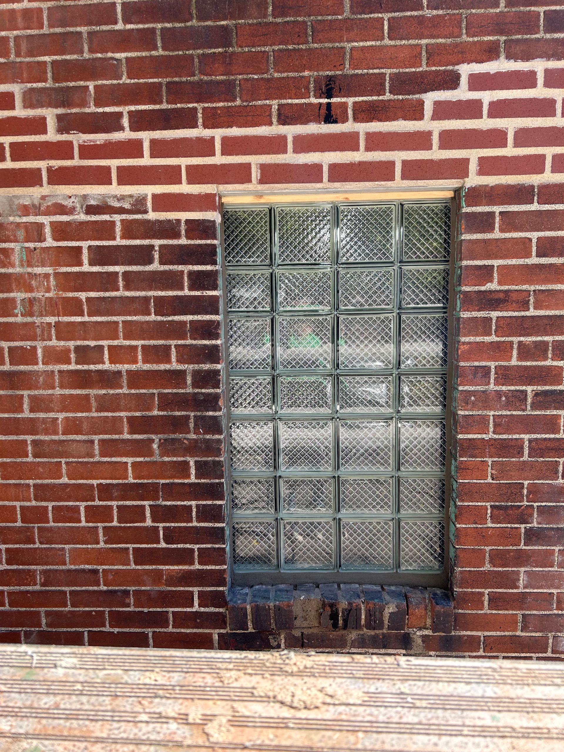 Red brick wall with a glass block window; weathered texture.