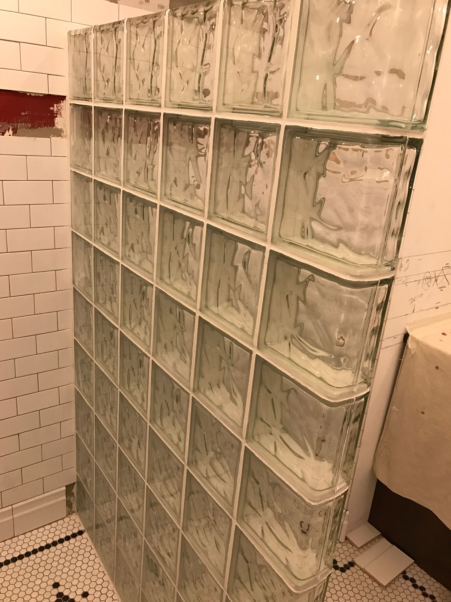 Glass block wall in a bathroom, with white grout lines and black and white patterned floor tiles.