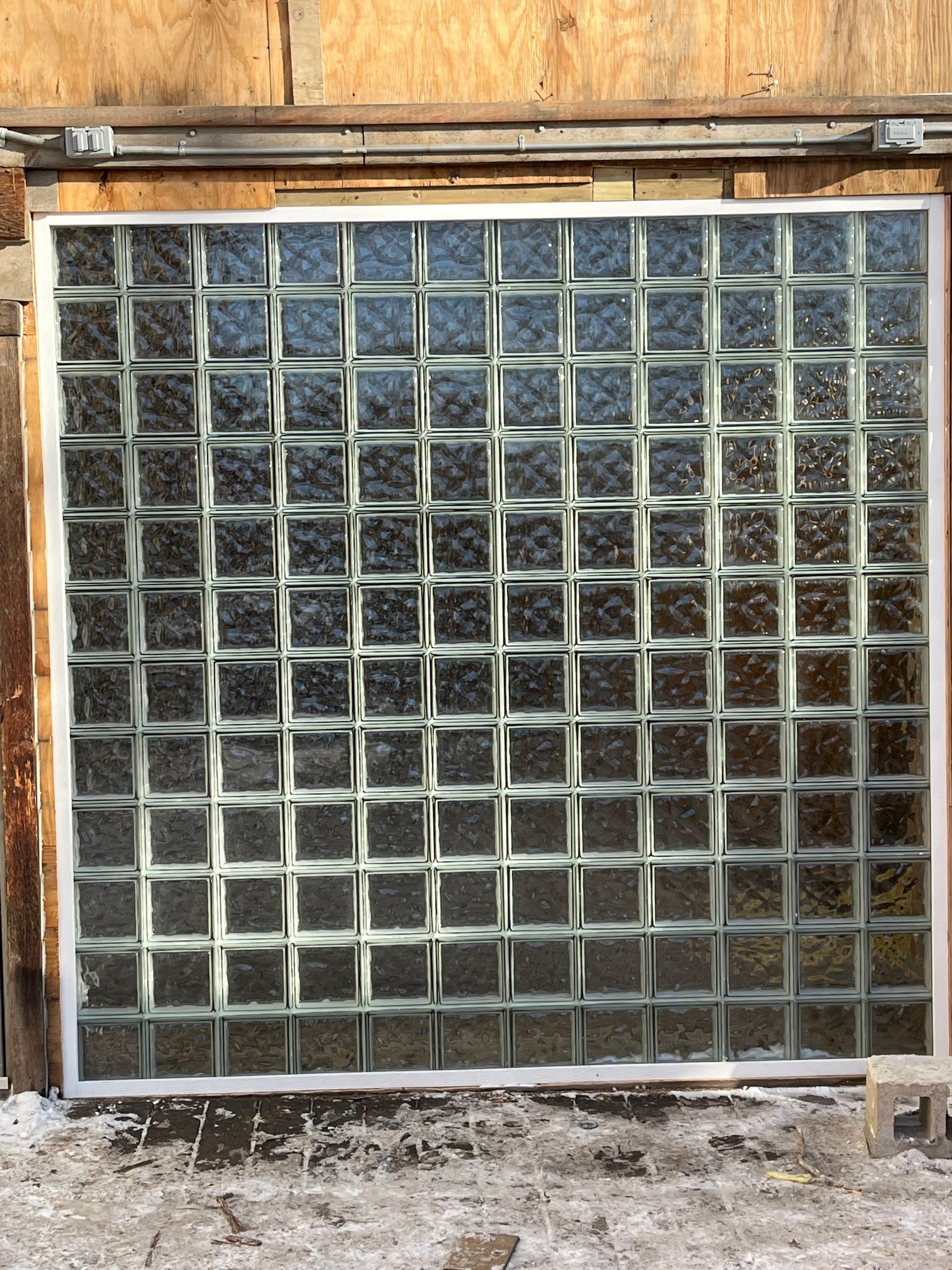 Glass block window set into a wooden exterior wall, with visible snow in the foreground.