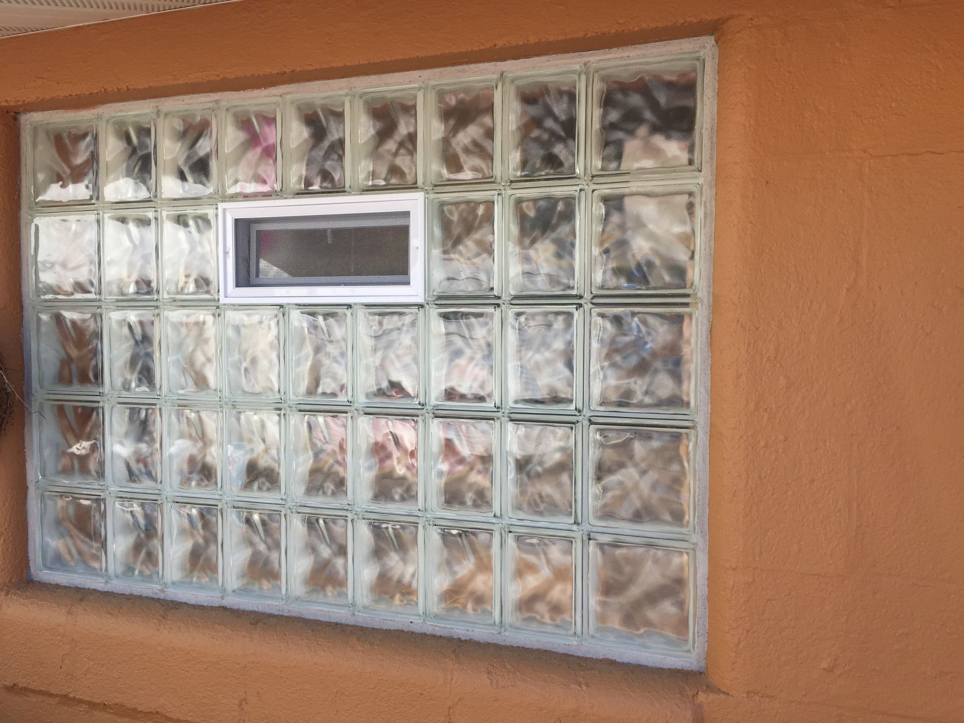 Glass block window in an orange stucco wall; small white window centered.