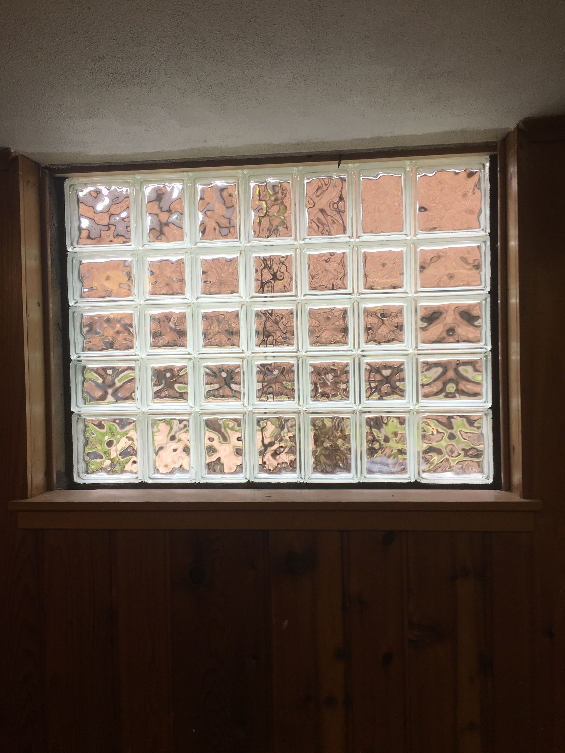 Glass block window set in wooden frame, viewed from inside a room with wood paneling.