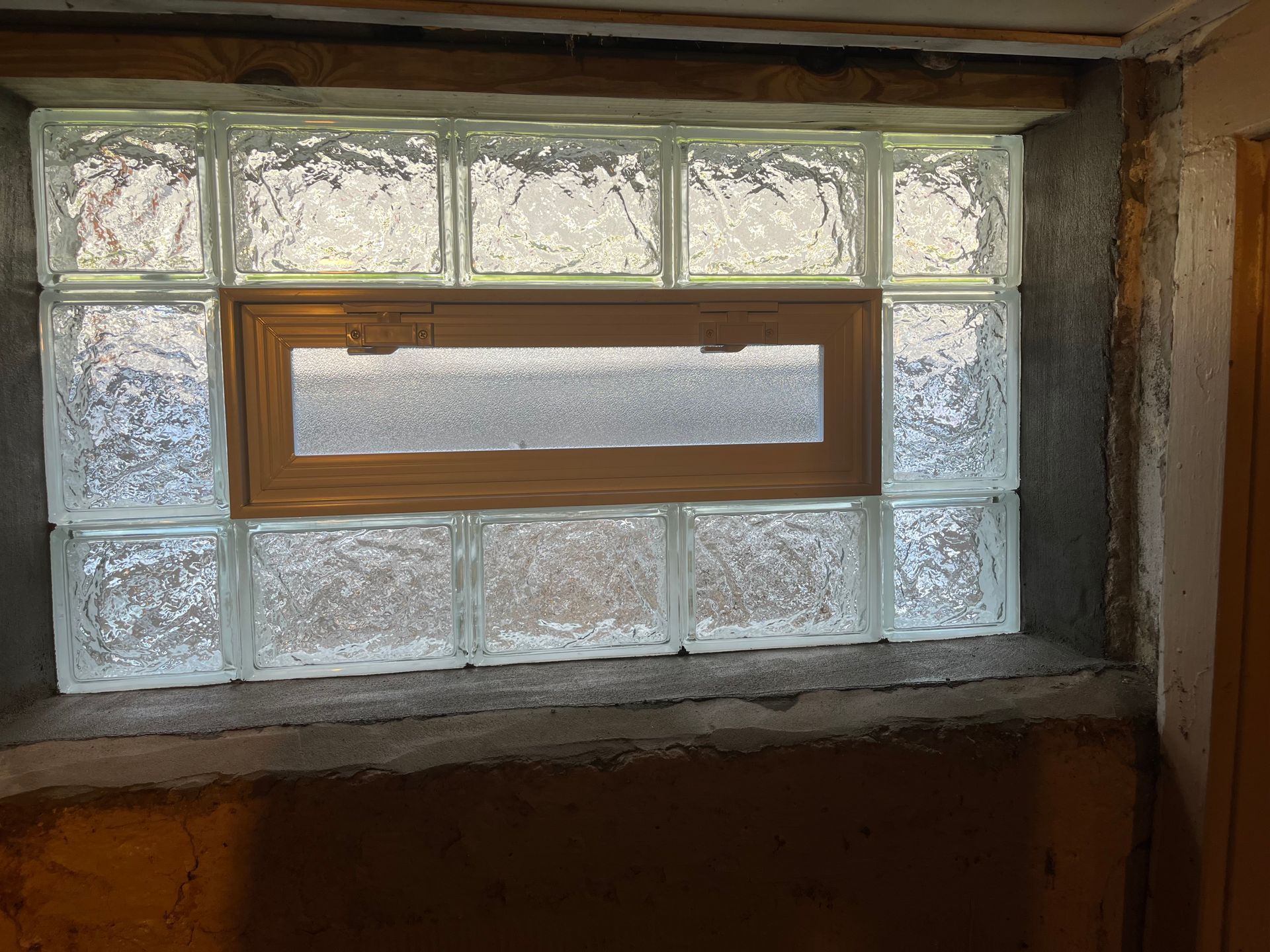 Glass block window with a rectangular wooden window in the center, set in a concrete basement wall.