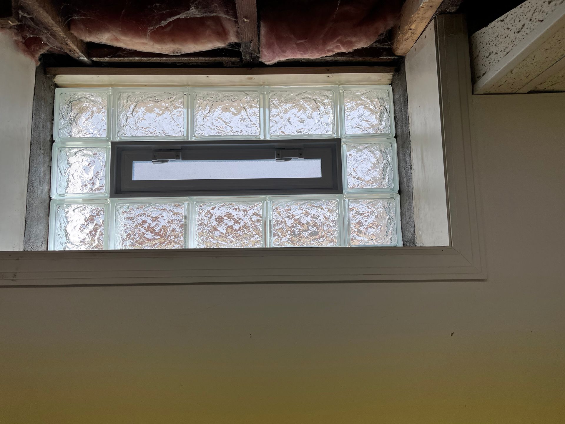 Glass block window with a smaller opening section, set in a white frame in a basement.