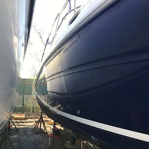 Dark blue boat hull next to a white boat, on stands, outdoors.