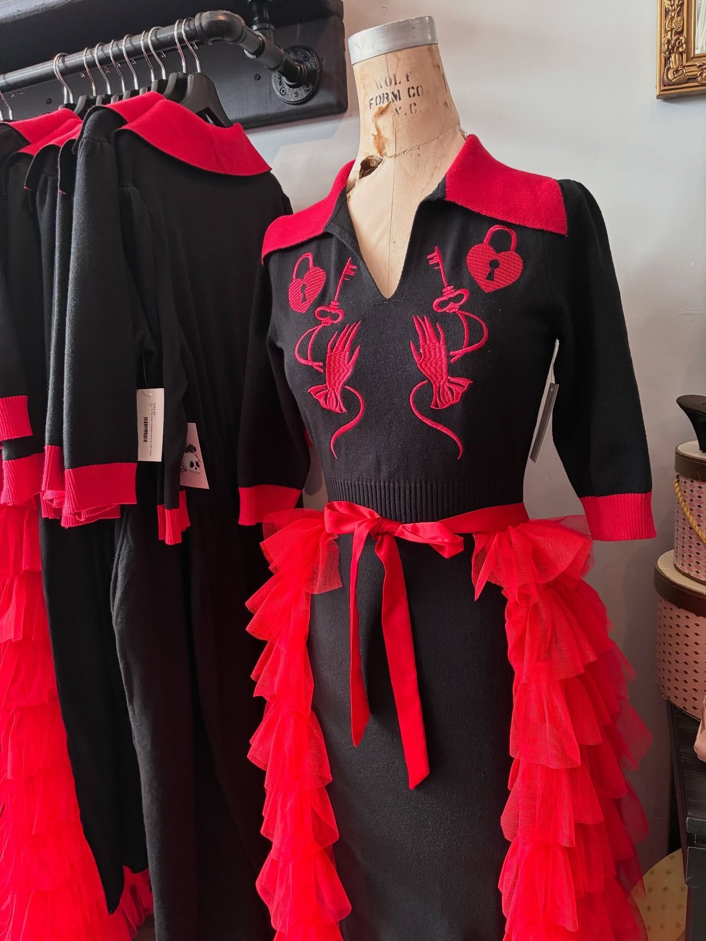 Black dress with red collar, embroidered design, and tiered red tulle trim; on a mannequin