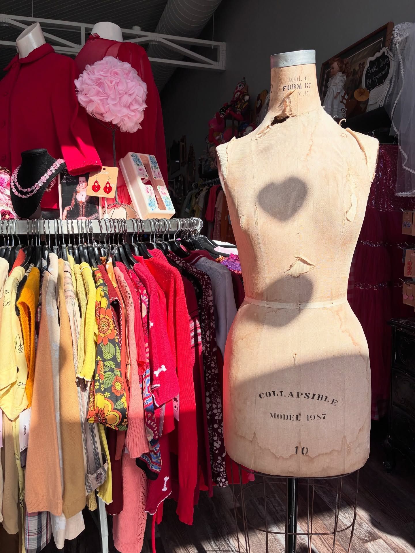 Vintage dress form in front of a clothing rack filled with colorful clothes