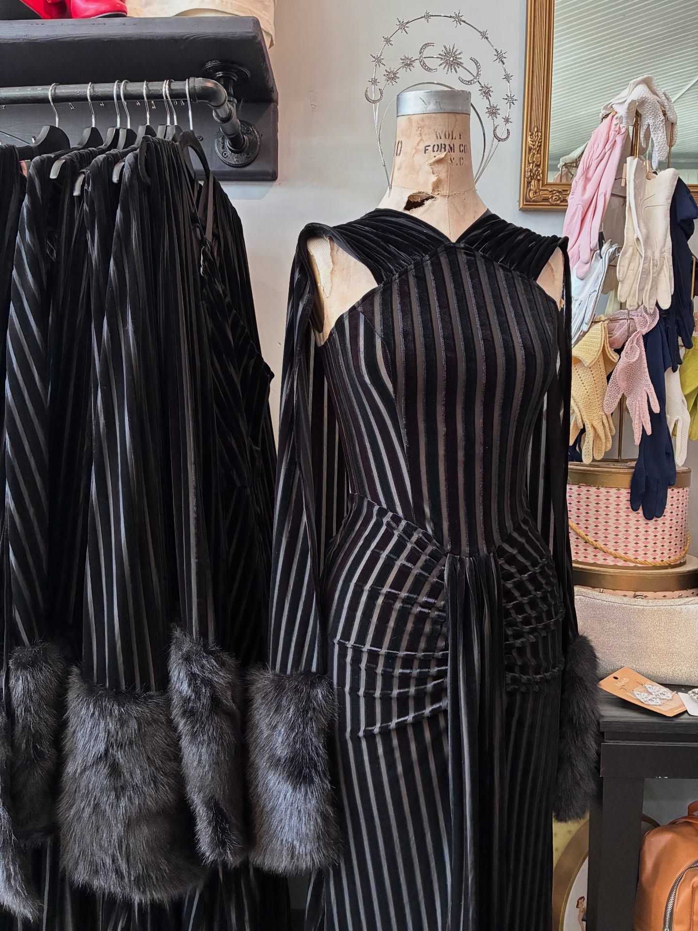 Black striped dress with fur cuffs on a mannequin, with coats hanging beside it