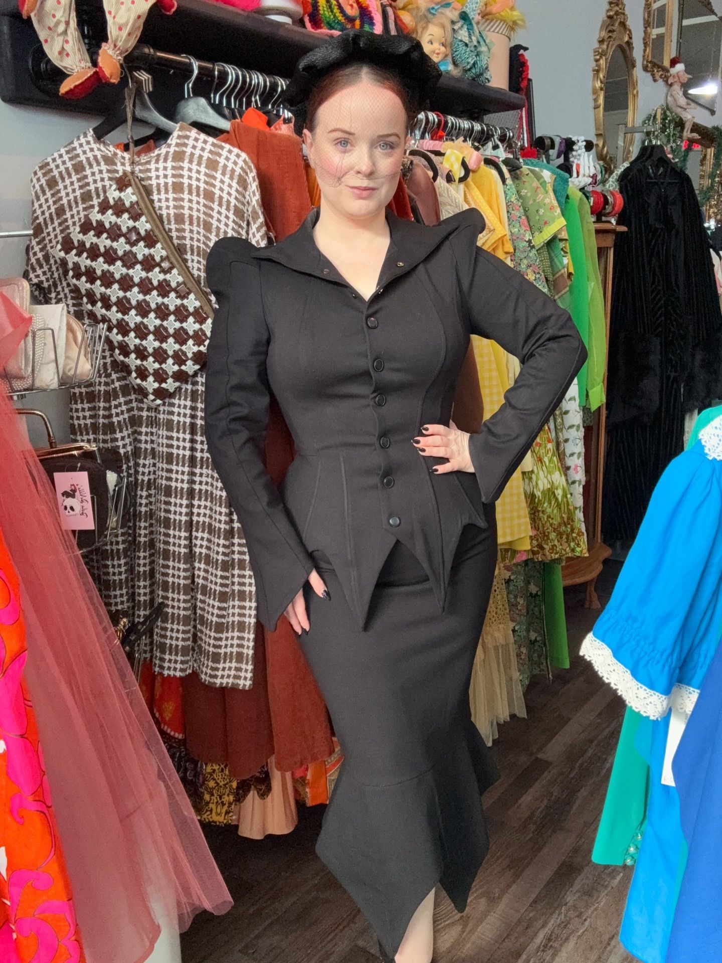 Woman in a black suit poses in a vintage clothing store