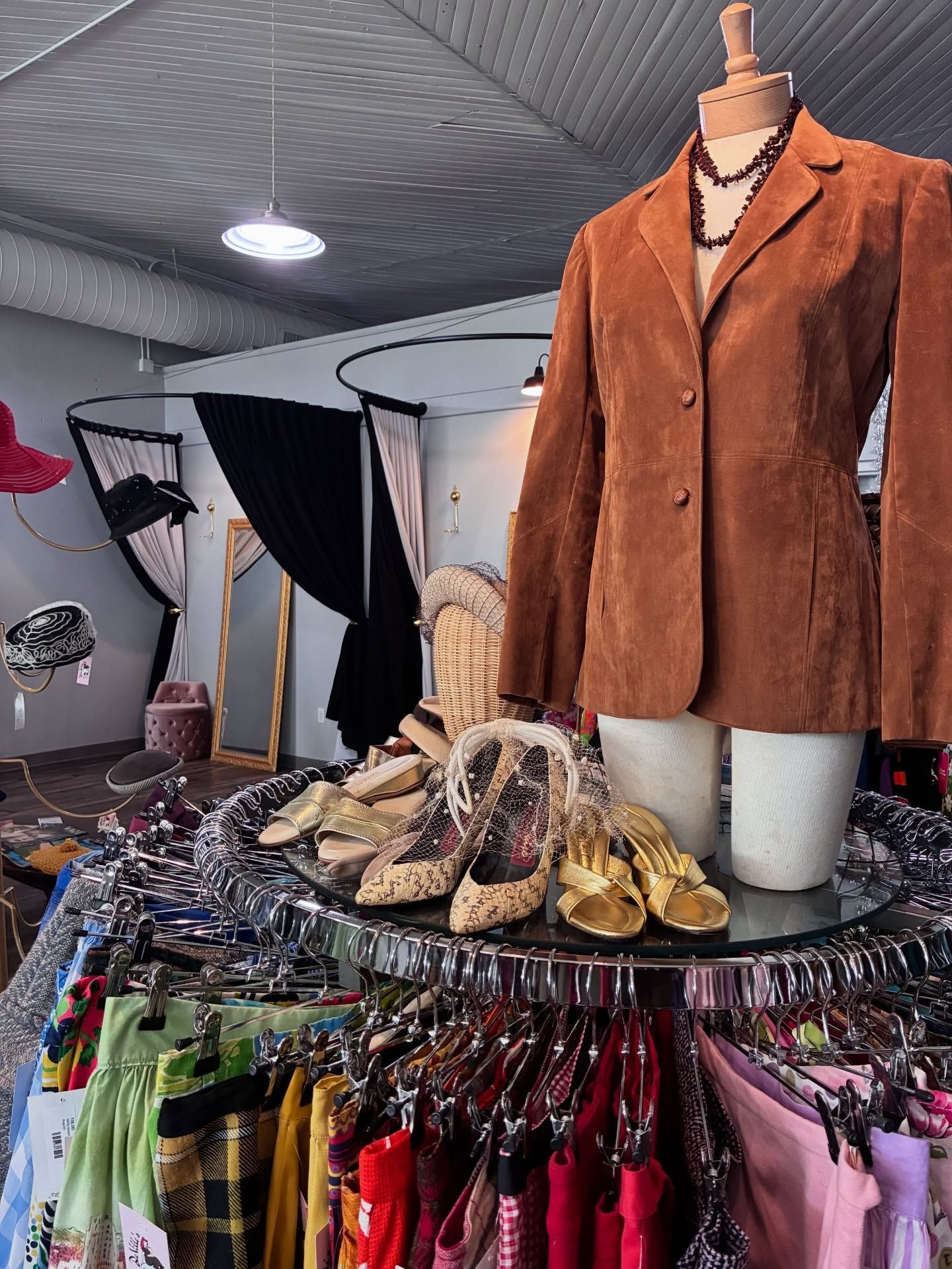 Clothing boutique interior: brown suede jacket on a mannequin, racks of colorful clothes, shoes on a mirrored display
