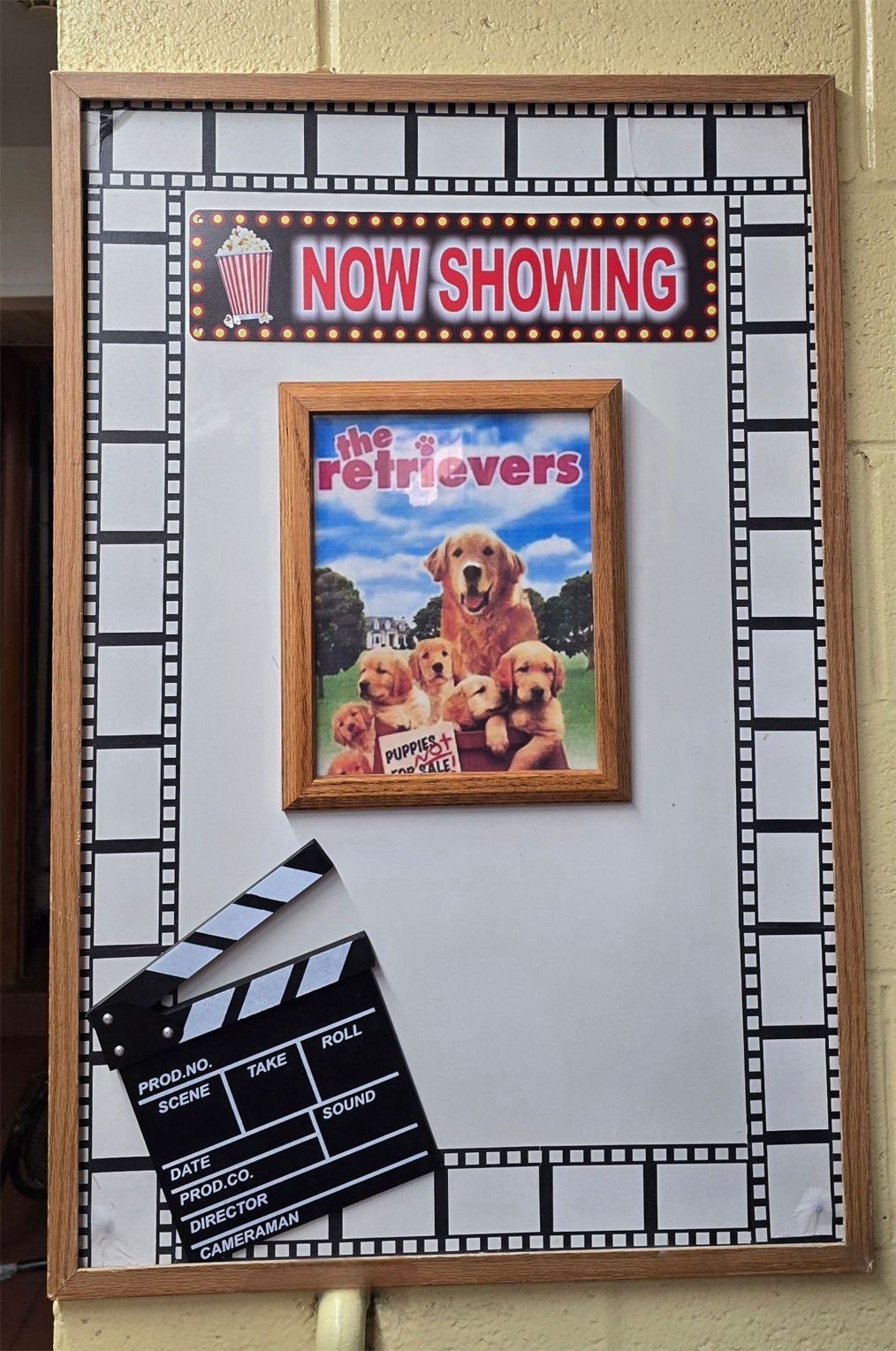 Framed movie-themed display with a Now Showing sign, The Retrievers poster, and a clapperboard