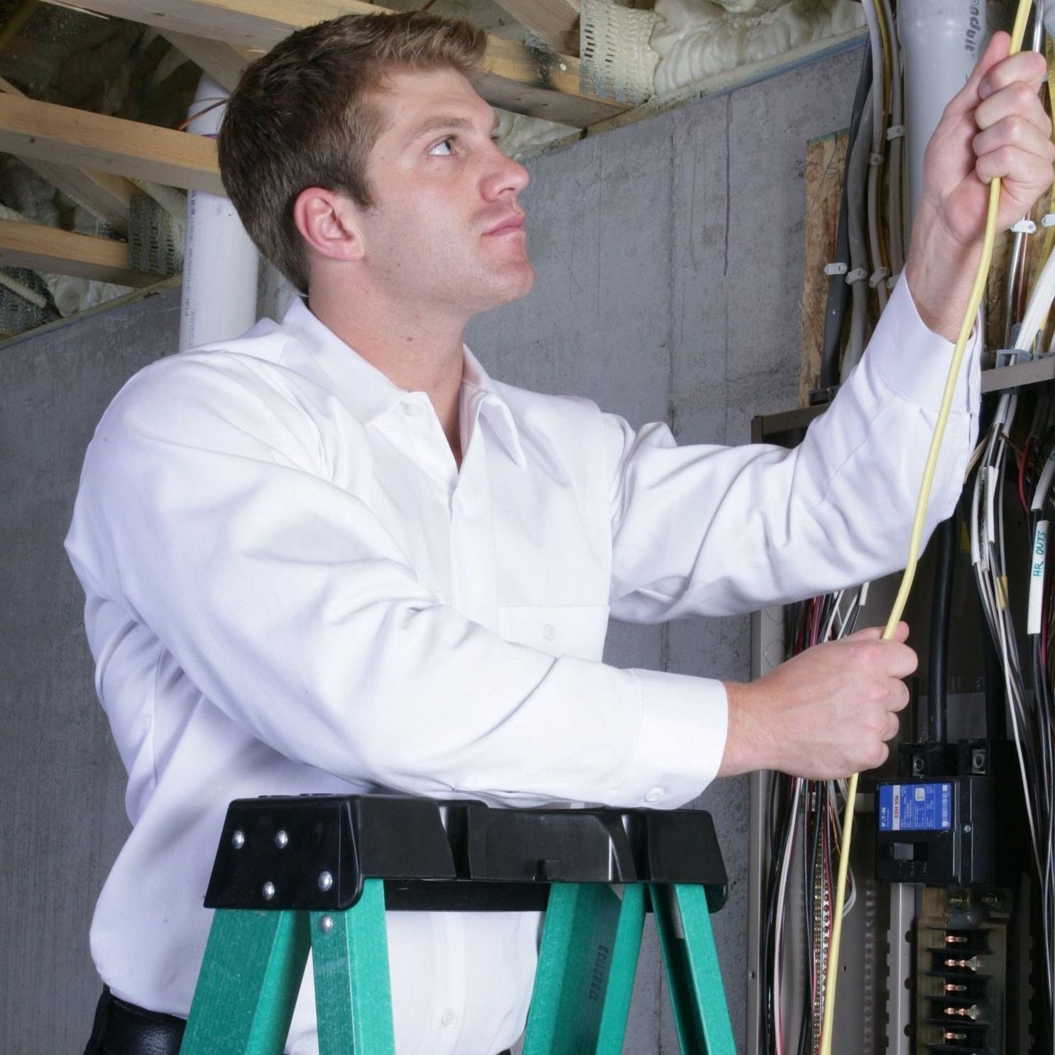 a man standing on a ladder measuring a wire