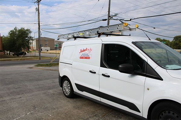 White service van parked by a street with ladder racks on top near power lines.