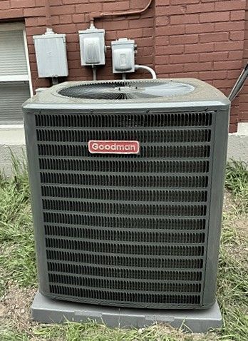 Goodman outdoor air conditioner unit beside a brick house and utility meters.