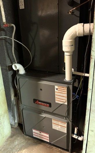 Two gray furnace units in a basement utility area with white PVC pipes and exposed ducting.