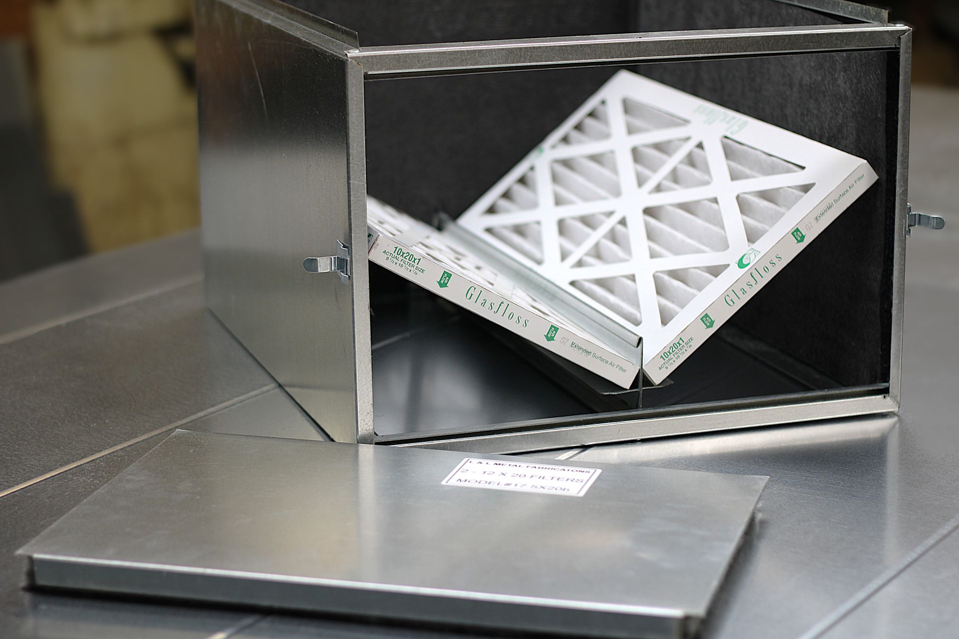 White lattice-shaped object inside a metal box with an open lid on a work surface.