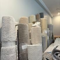 A large stack of rolled-up, varying textured carpets in a light-colored room.