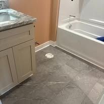 Bathroom with a white bathtub and vanity with light-colored cabinetry. The floor is gray with a speckled pattern.
