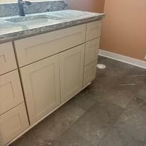 Bathroom vanity with light-colored cabinets and a granite countertop. The floor is covered in dark gray tiles.