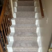 Staircase with light gray carpet and white painted risers, wooden banister on the left, leading upwards.