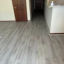 A wooden floor in a home with a closed door and a kitchen counter. The floor has grey wood-like planks.