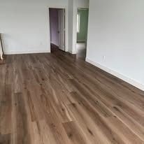 Hardwood floor in a room, leading towards an open doorway. Sunlight highlights the planks' grain and color.