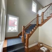 Staircase with blue carpet and wooden banister, leading up to a window in a light-colored room.