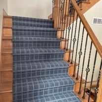 Staircase with a dark blue checkered carpet, wooden steps, and a decorative wrought iron railing.