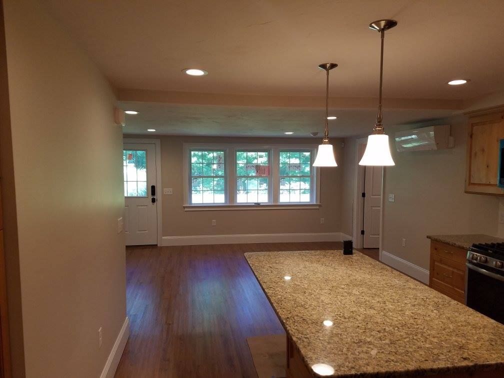 Interior view of a kitchen with island and three hanging lights; tan walls, hardwood floors, windows.
