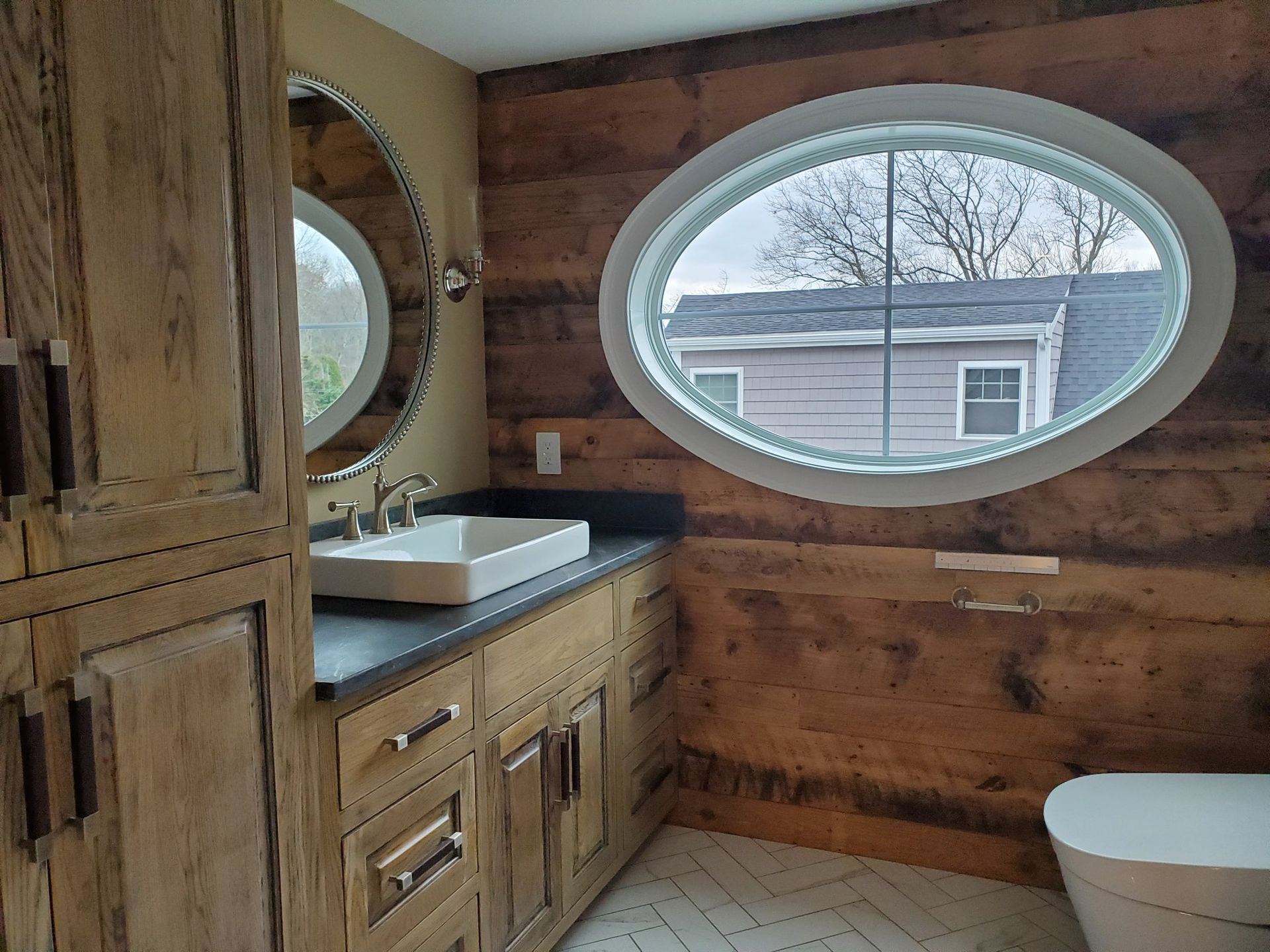 Bathroom with wood-paneled walls, oval window, and vanity with a dark countertop and white sink.