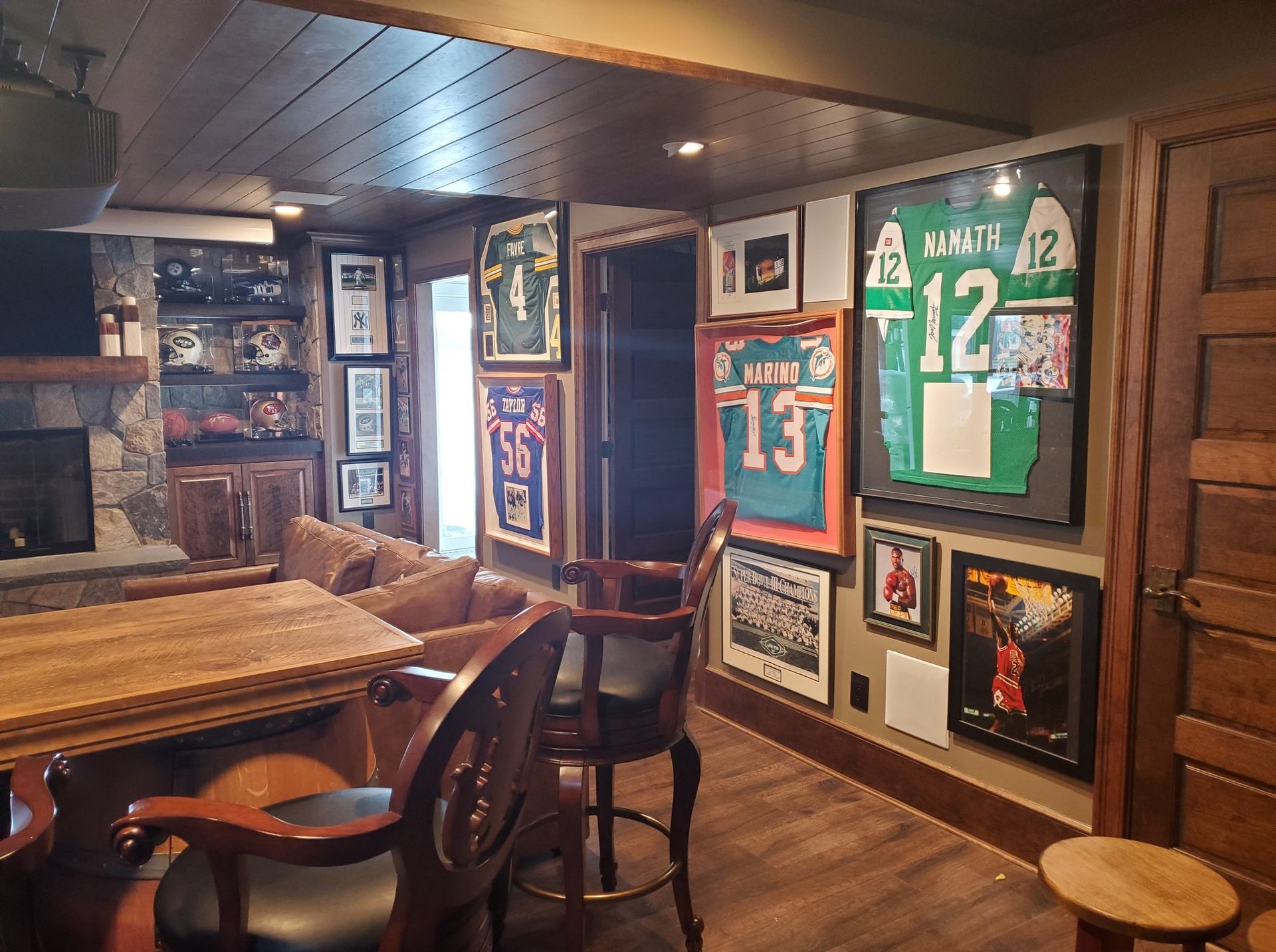 A sports-themed man cave with framed jerseys, bar seating, a fireplace, and wooden accents.