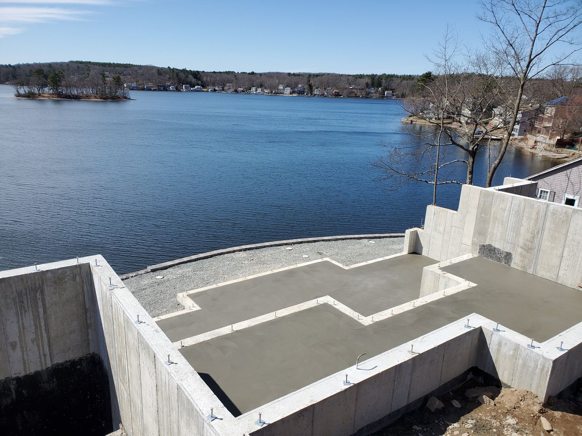 Construction site with concrete foundation overlooking a lake with blue water and a bright sky.