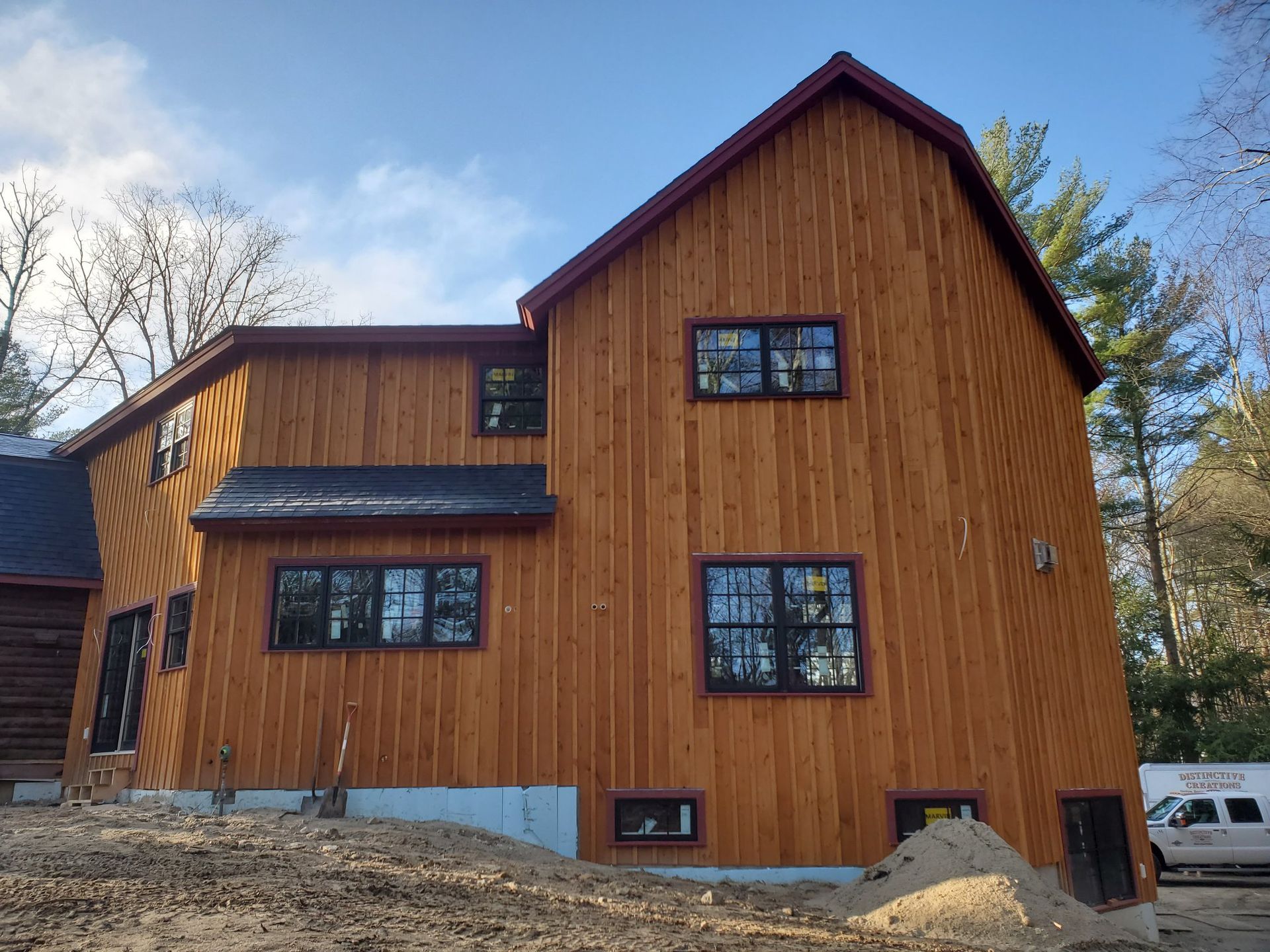 Wood-sided house with black-framed windows and a red roof trim against a blue sky.