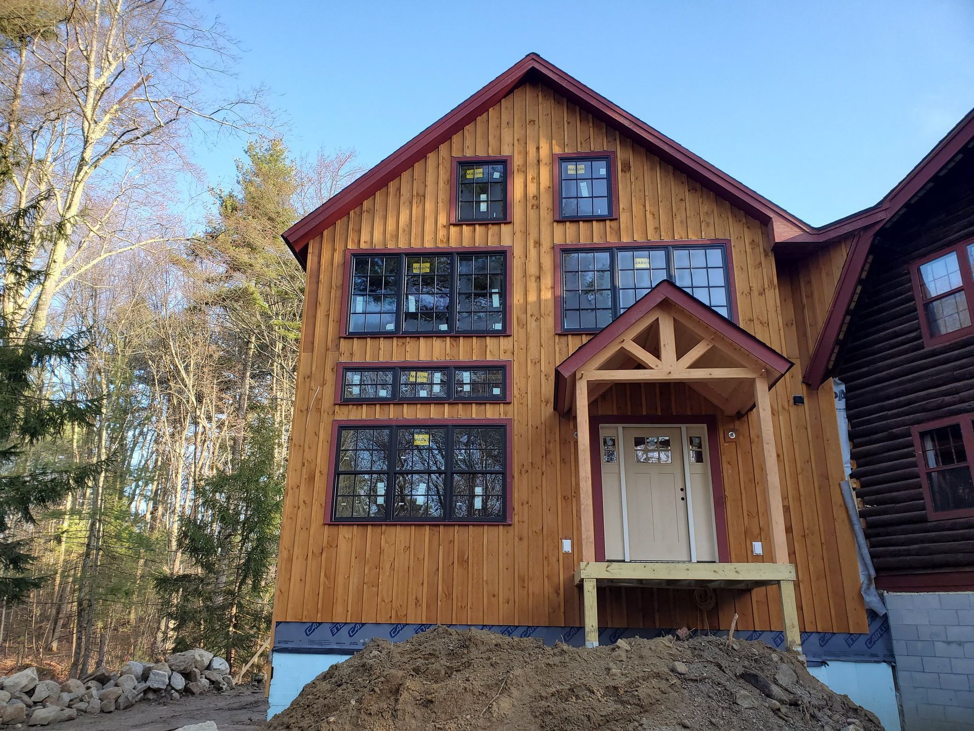 Two-story wooden house under construction with many windows, red trim, and a small porch.