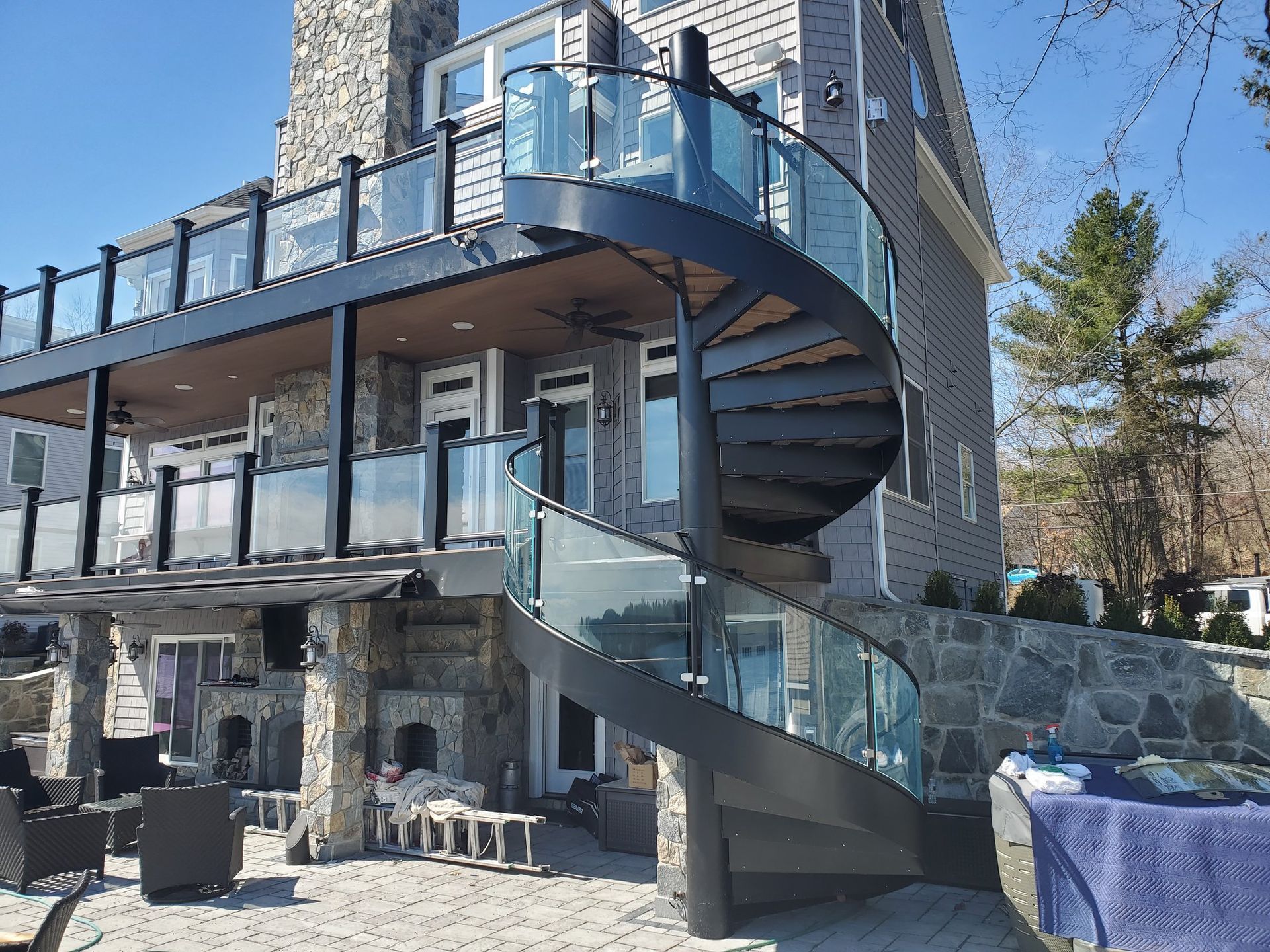 Black spiral staircase with glass railings on a gray house with stone accents.