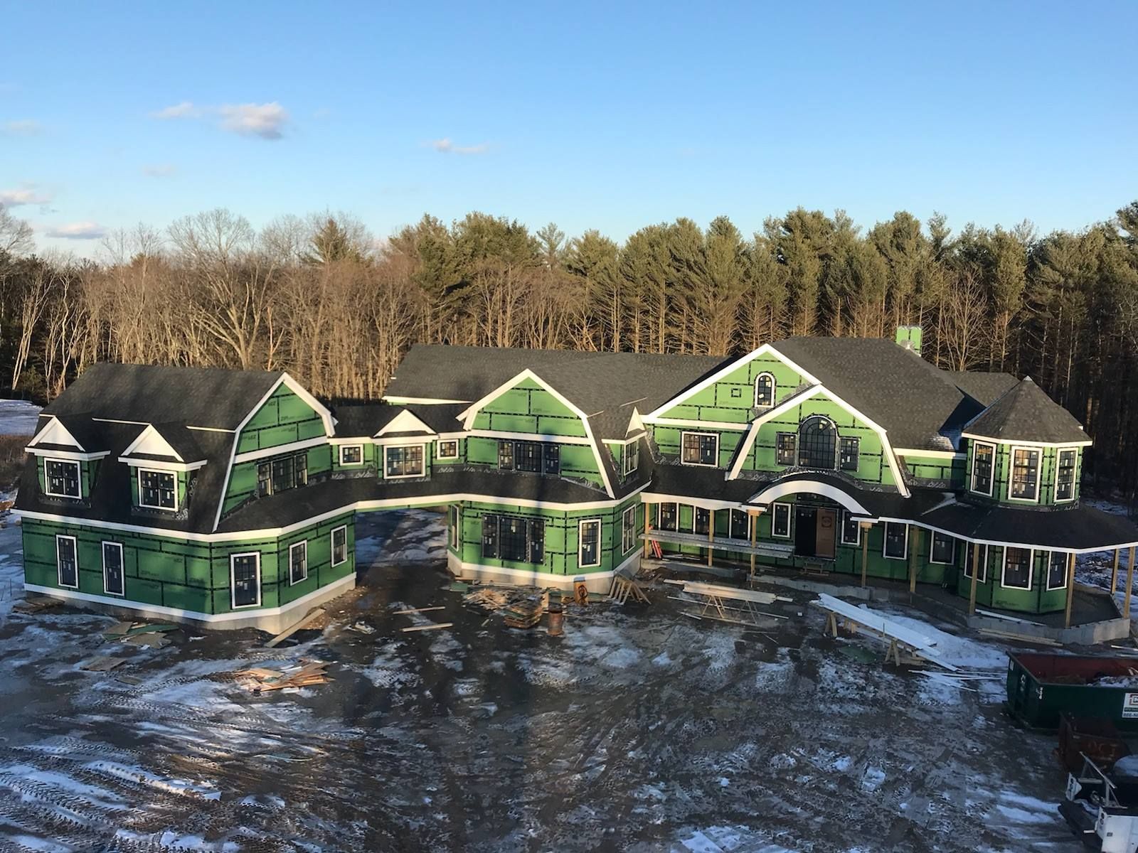 A large, new house under construction with green sheathing, black roof, and snow on the ground.