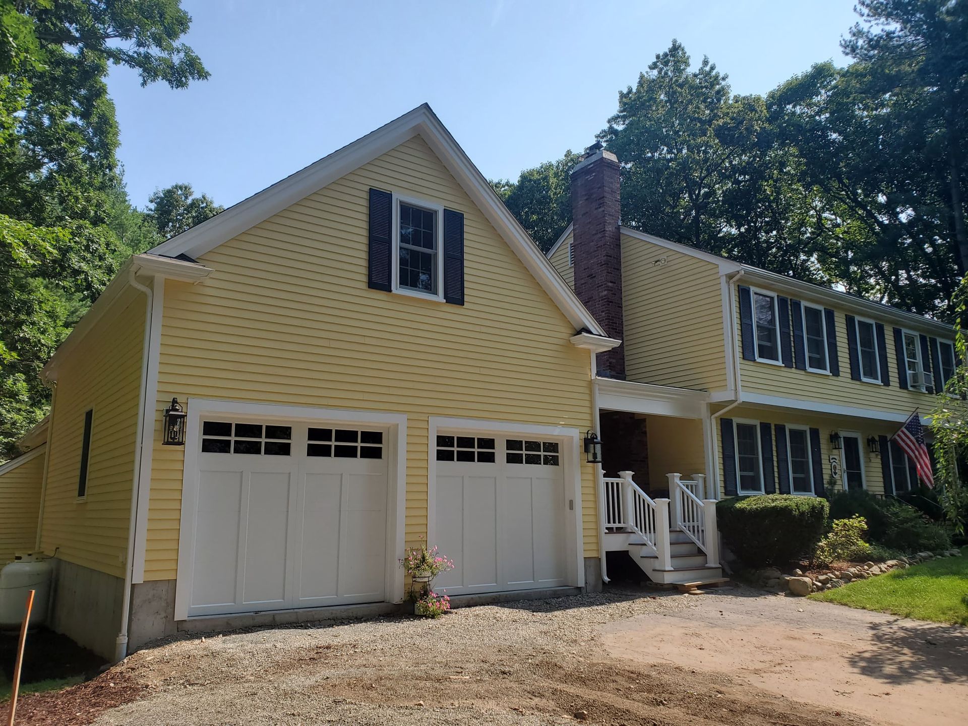 Yellow house with white garage doors and black shutters; brick chimney.