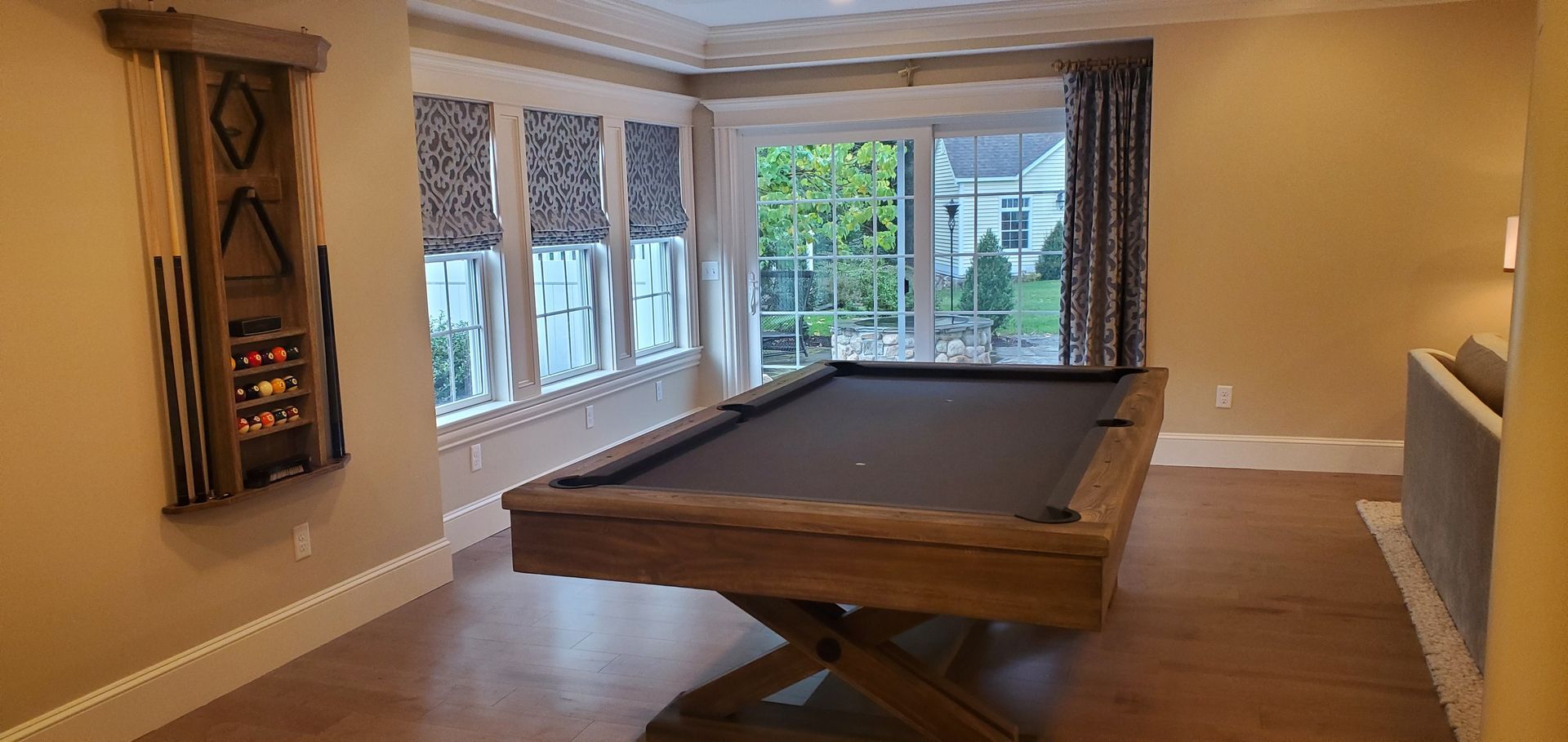 A pool table in a room with windows and a cue rack on the wall.