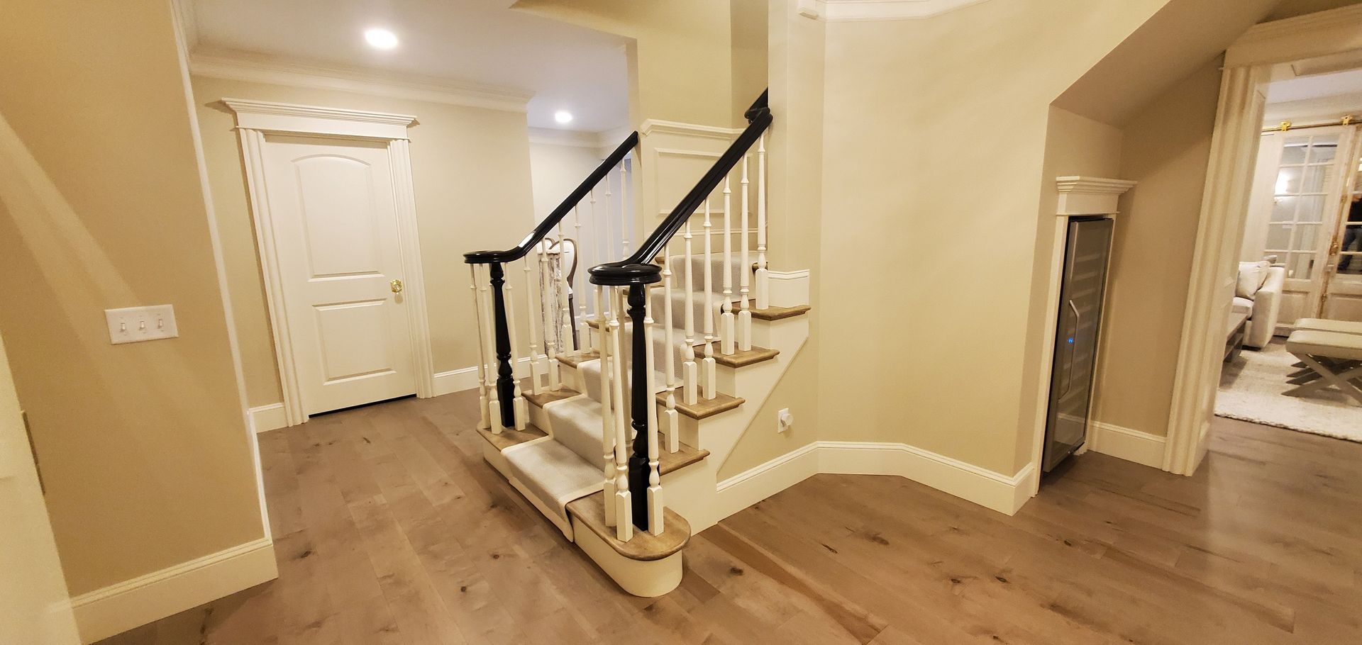 A beige-walled entryway with wooden floors, staircase, and white door.