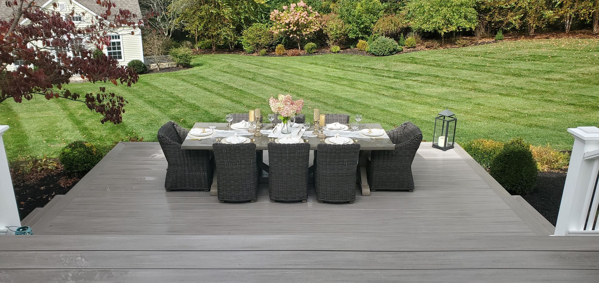 Outdoor dining set on a wooden deck, with a lush green lawn in the background.