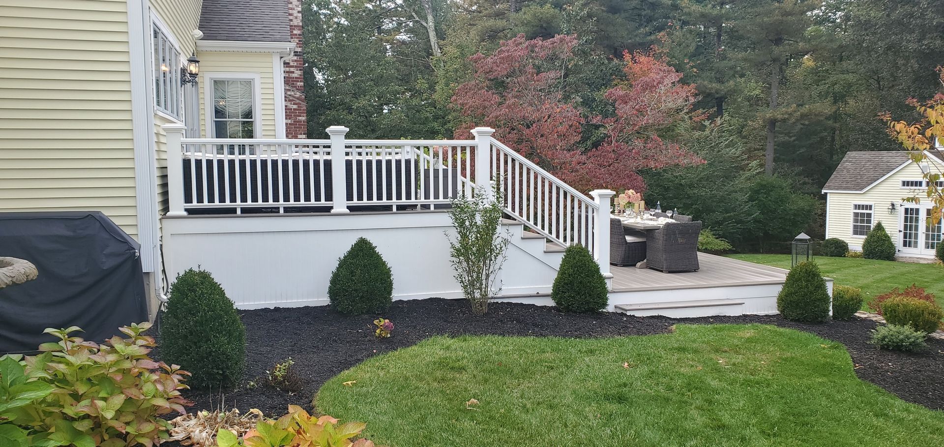 Backyard deck with white railing and landscaping featuring a lawn, shrubbery, and a small playhouse.