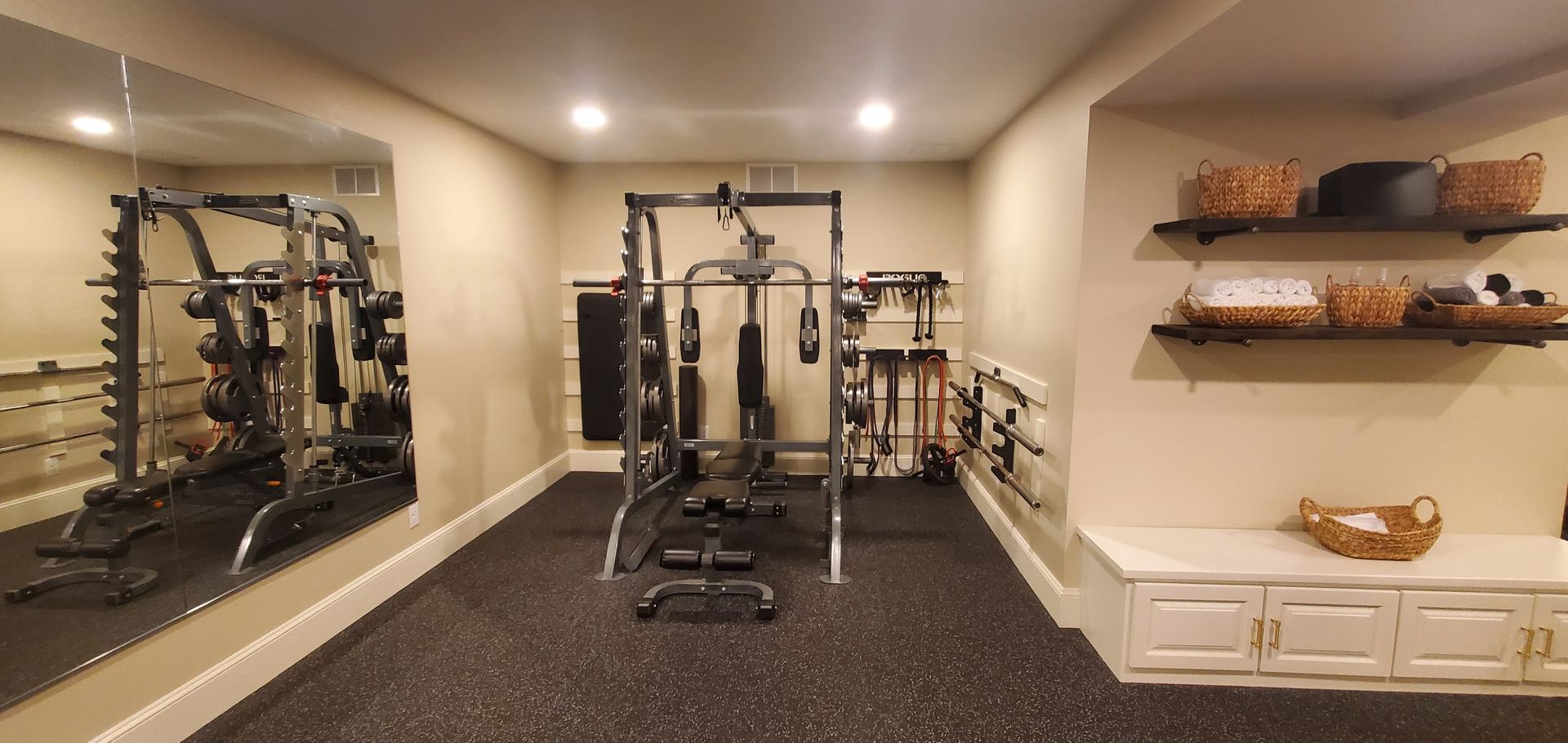 A well-equipped home gym with exercise machines, weights, mirrors, and storage shelves.