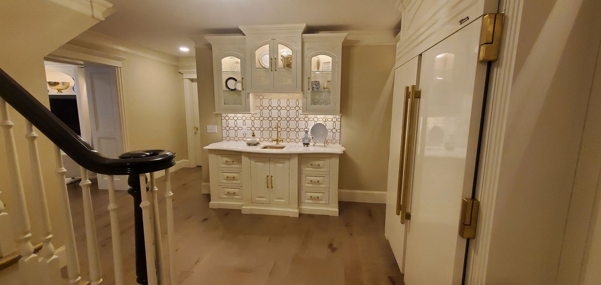 A white kitchen with cabinetry, drawers, and a tiled backsplash, next to a staircase.