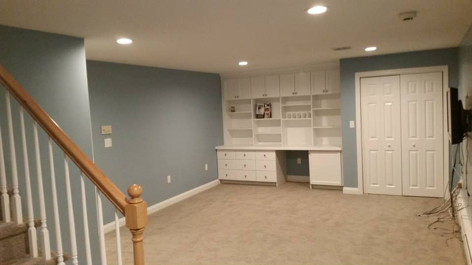 Basement with blue walls, built-in white desk/shelves, and white closet. Beige carpet, wooden stairs.