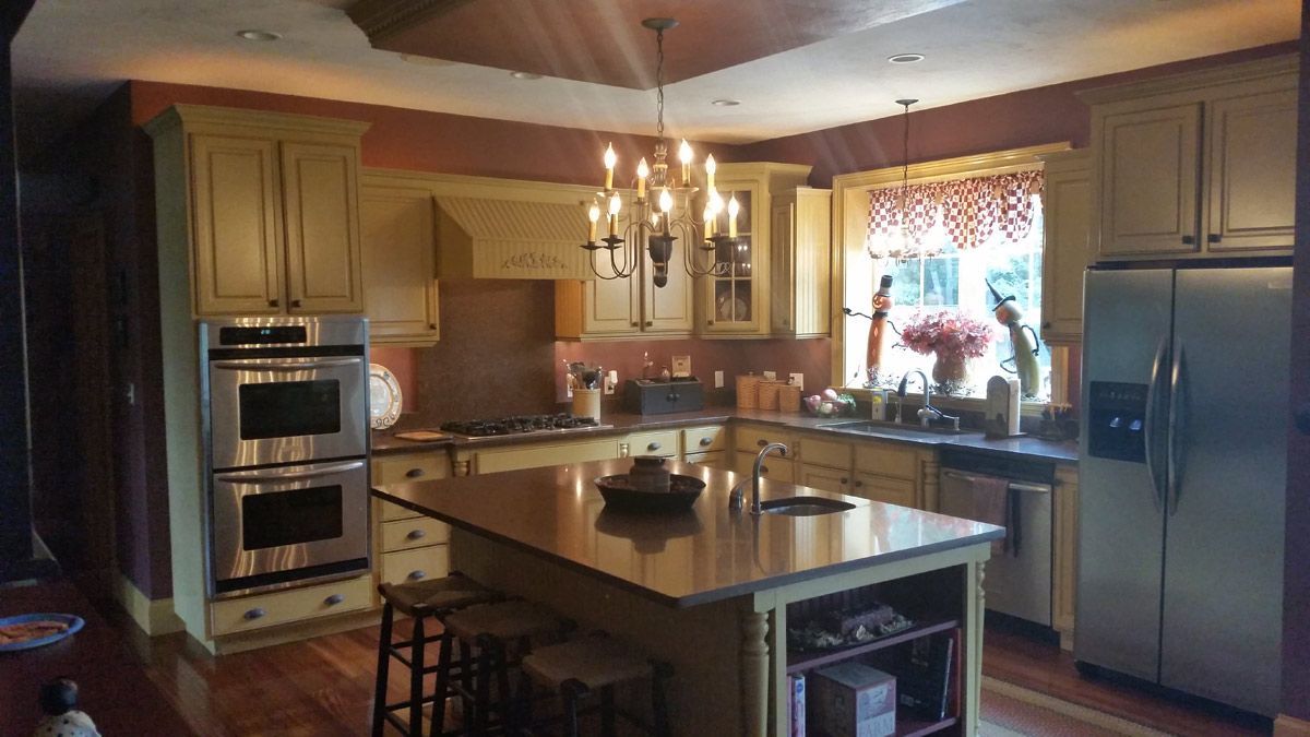Yellow-painted kitchen with stainless steel appliances, island with stools, and chandelier.