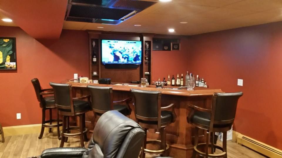 Basement bar with red walls, wooden bar & stools, TV, and a black leather recliner.