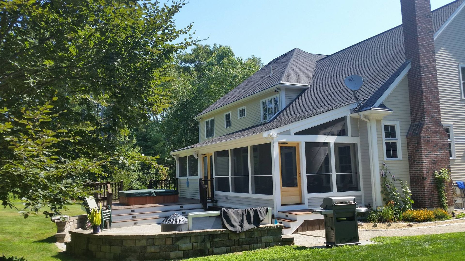 Backyard with a two-story house, screened porch, patio, brick chimney, and green lawn on a sunny day.