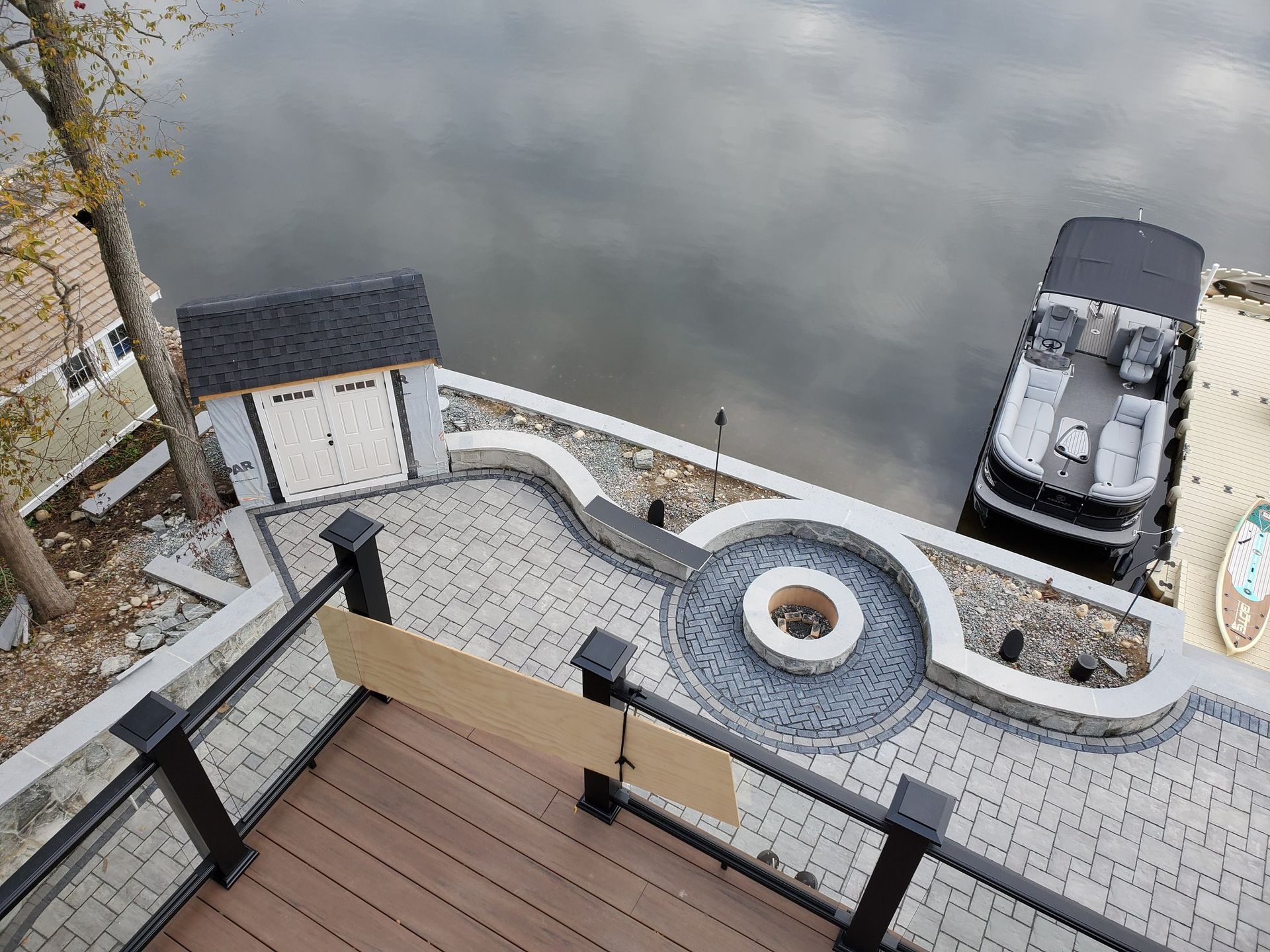 Overhead view of a waterfront deck with a fire pit, shed, and boat.