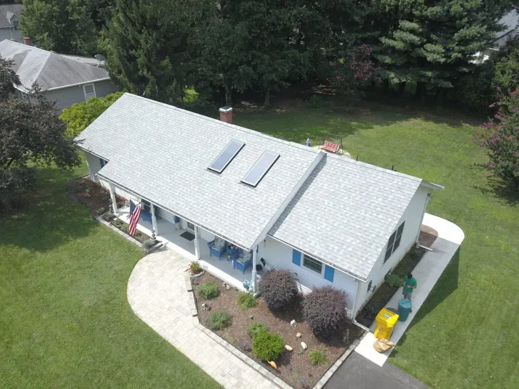 Aerial view of a light-gray house with a green lawn and landscaped yard.